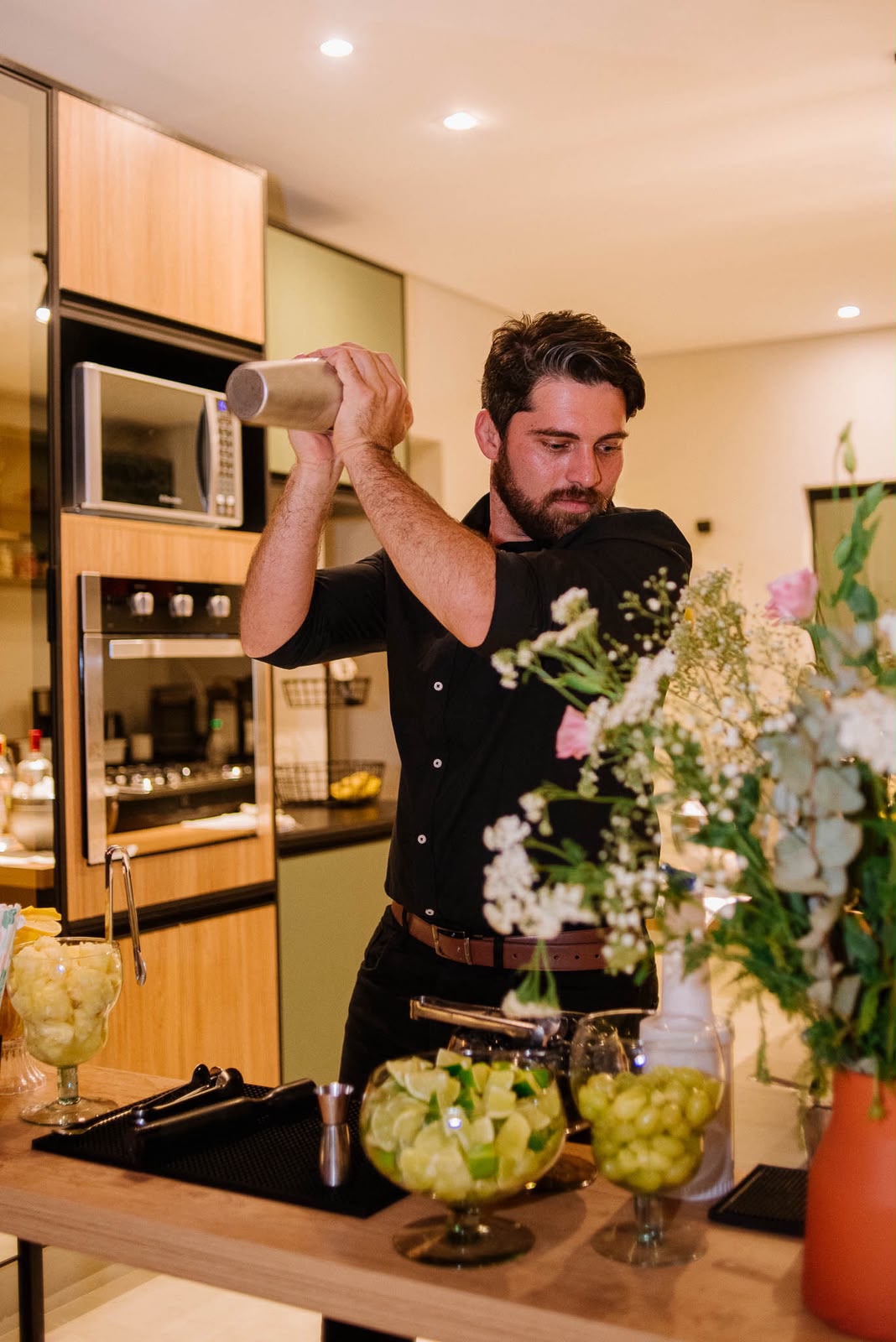 Barman preparando um drink na coqueteleira, ao lado de arranjo de flores