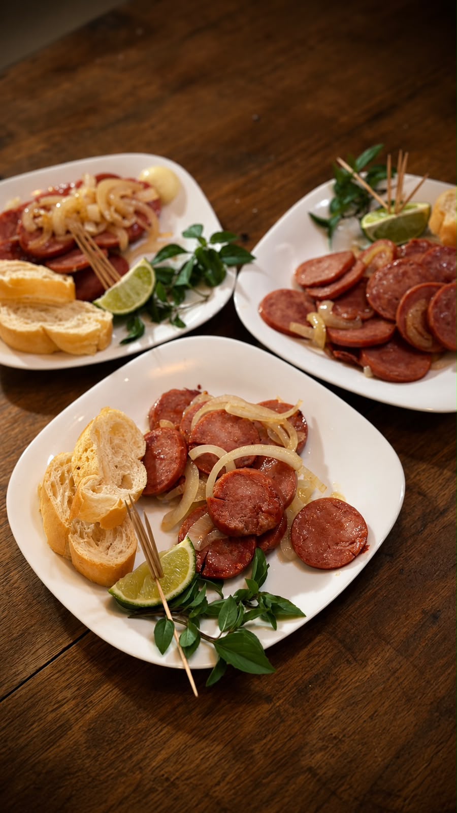Pratos de linguiça acebolada com pão e limão sobre mesa de madeira