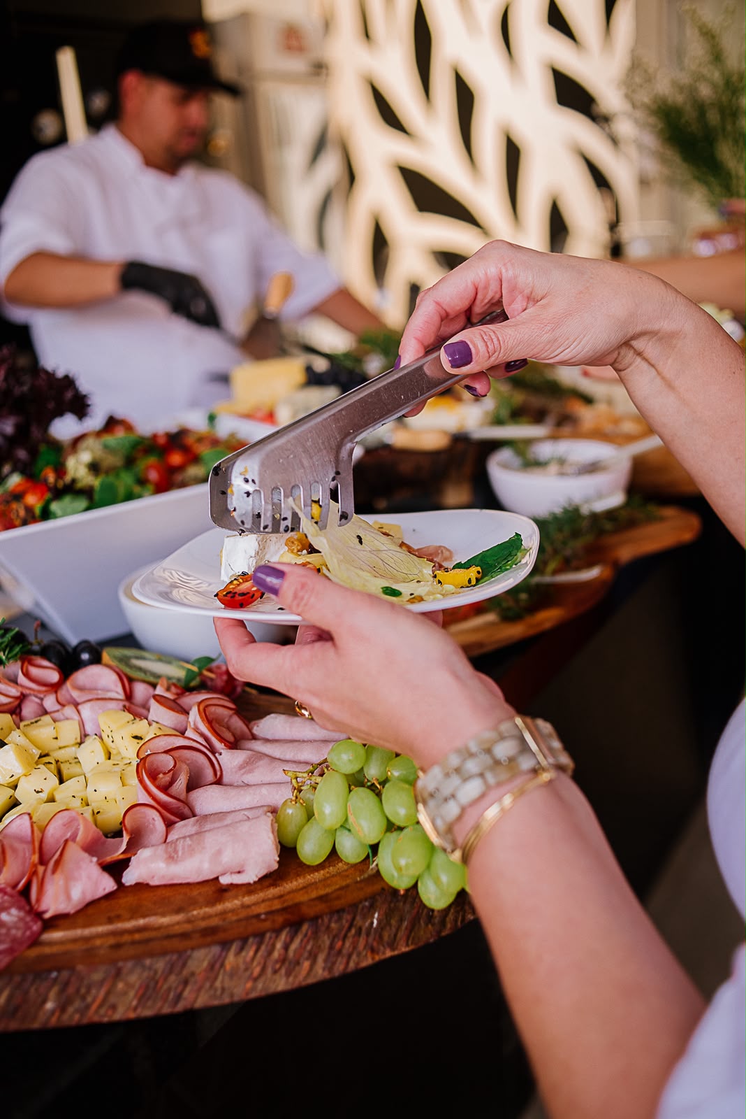 Convidada se servindo de frios, queijos e uvas na mesa do buffet