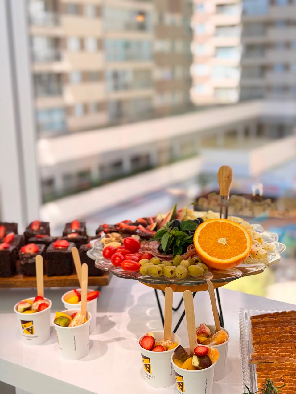 Mesa de coffee break com frios, frutas, brownies e copinhos de frutas