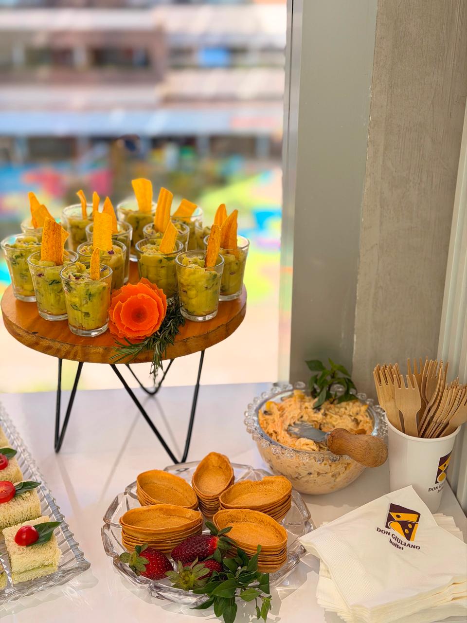 Mesa de coffee break com copinhos de frutas, salgados e sanduíches