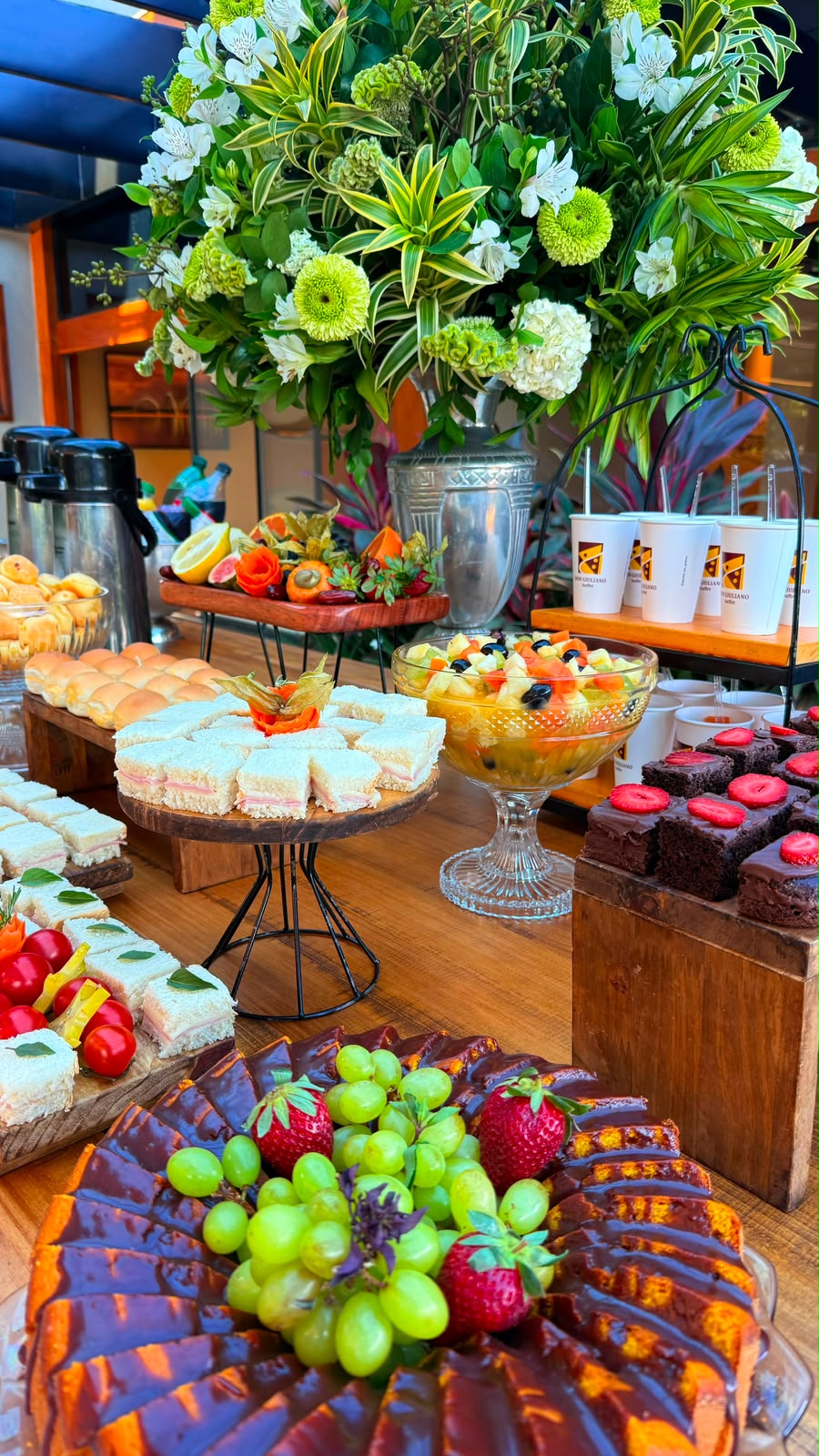 Mesa de lanche com sanduíches, frutas, doces e arranjo de flores