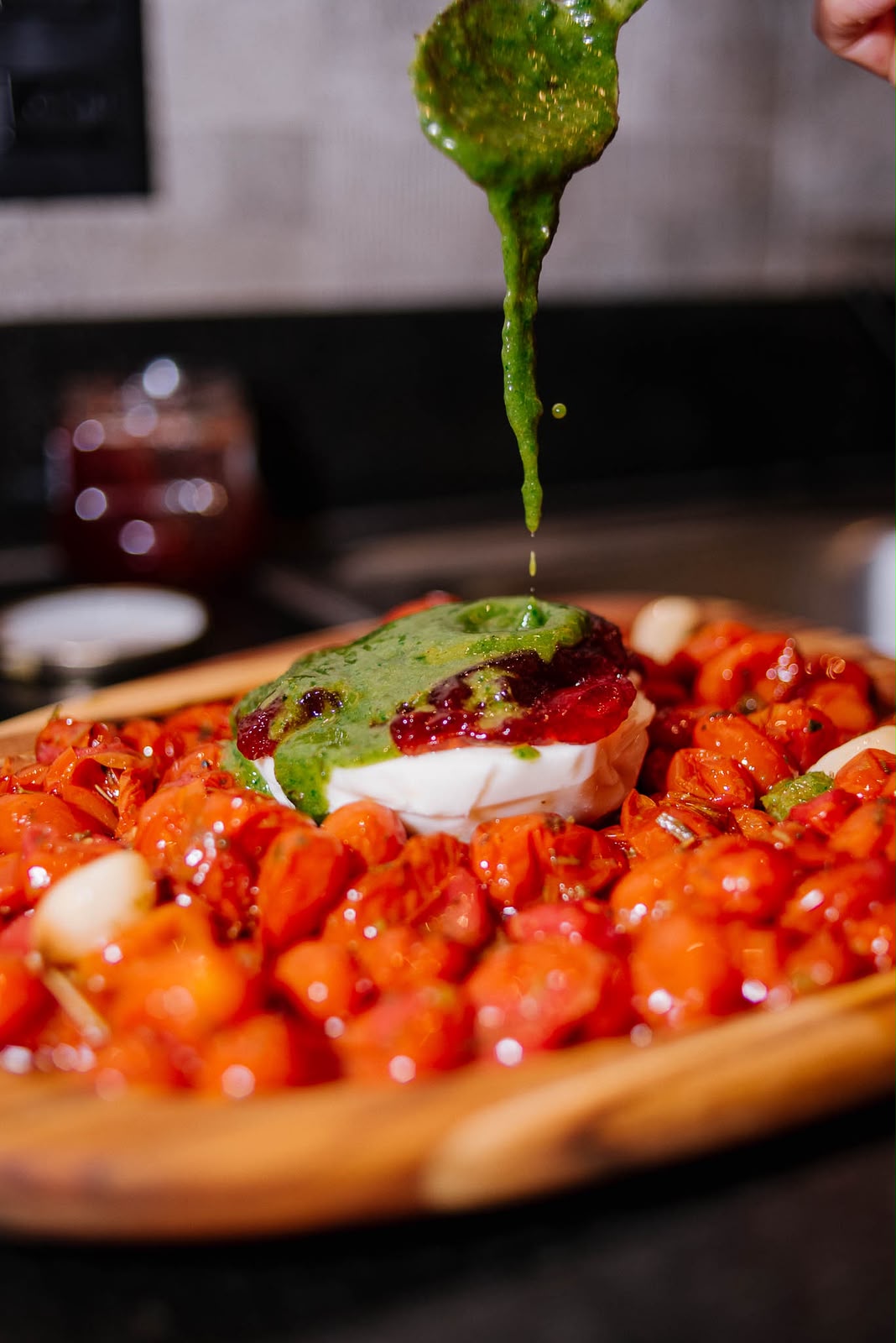 Molho verde sendo finalizado sobre burrata com tomates na tábua
