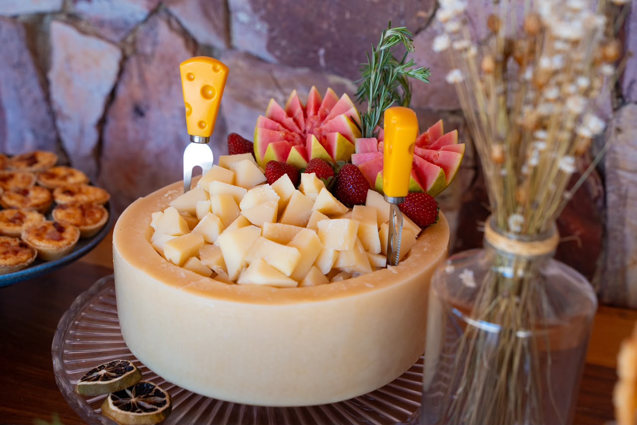 Queijo em cubos servido dentro de uma peça de queijo, com frutas e tortinhas ao redor
