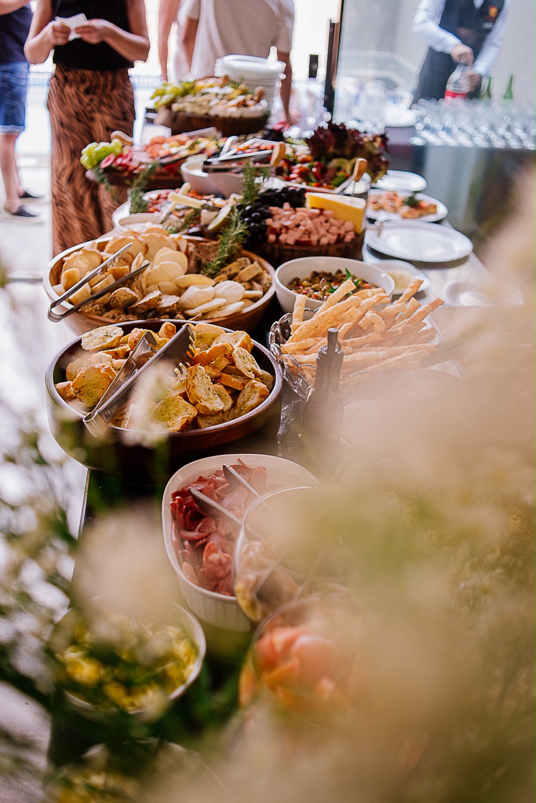 Mesa de buffet montada no salão com cestas de pães, frios, saladas e pastas