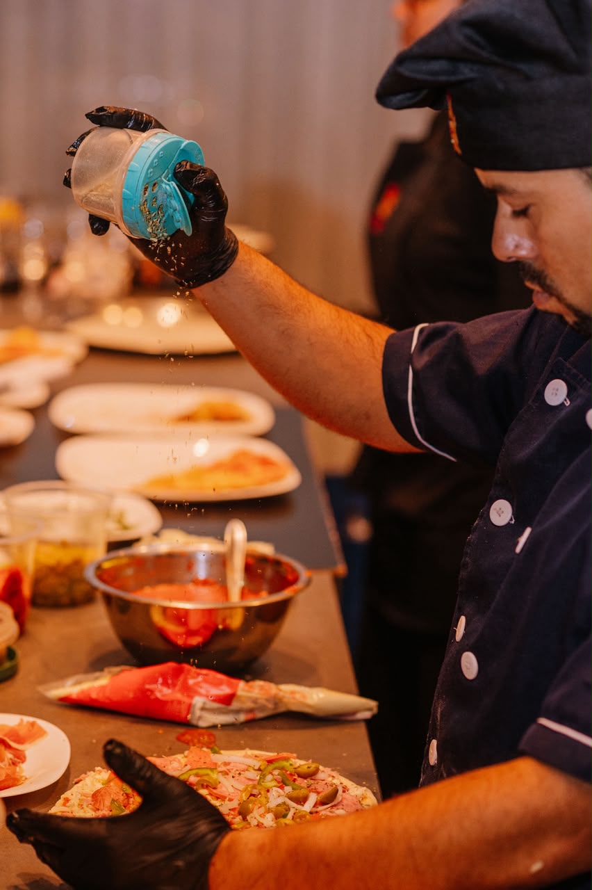 Pizzaiolo finalizando pizzas na bancada durante um evento
