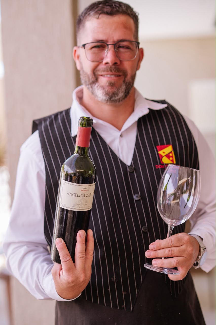 Garçom sorrindo com uma garrafa de vinho e uma taça